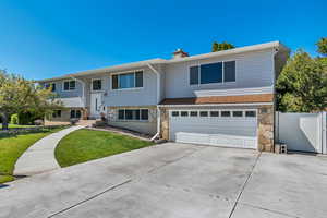 Split foyer home with stone siding, an attached garage, a chimney, a front lawn, and driveway