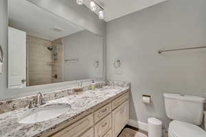 Bathroom featuring toilet, baseboards, tiled shower, and a sink