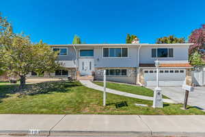 Raised ranch featuring concrete driveway, stone siding, a garage, and a front yard
