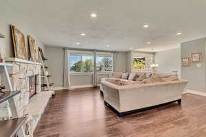 Living area featuring baseboards, a stone fireplace, recessed lighting, and dark wood-type flooring