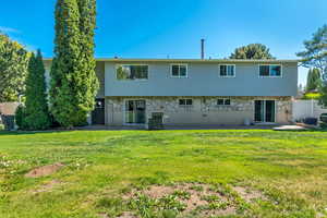 Rear view of house with a patio area, stone siding, and a lawn