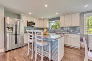 Kitchen with light wood-style floors, tasteful backsplash, white cabinetry, and appliances with stainless steel finishes