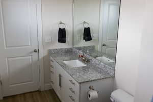 Half bathroom with toilet, wood finished floors, and vanity