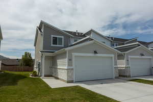 Multi unit property with fence, a garage, concrete driveway, stone siding, and a front lawn