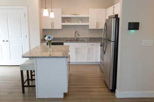 Kitchen featuring freestanding refrigerator, wood finished floors, white cabinets, and a sink