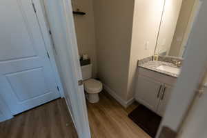 Half bathroom featuring vanity, toilet, baseboards, and wood finished floors