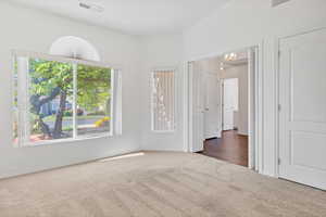 Unfurnished bedroom featuring carpet flooring, visible vents, baseboards, and a notable chandelier