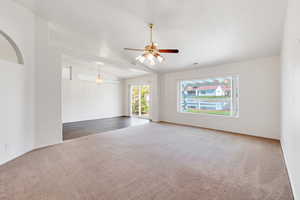 Unfurnished room with carpet, vaulted ceiling, ceiling fan, arched walkways, and baseboards