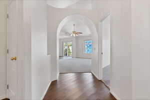 Hall with dark colored carpet, arched walkways, baseboards, and dark wood finished floors