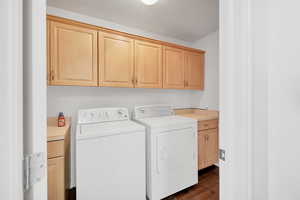 Washroom featuring dark wood finished floors, washer and dryer, and cabinet space