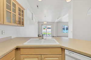 Kitchen featuring light brown cabinetry, glass insert cabinets, dishwasher, a sink, and light countertops