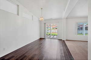 Unfurnished dining area with dark wood-style flooring, a notable chandelier, a healthy amount of sunlight, and vaulted ceiling