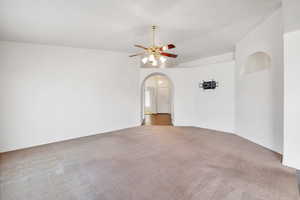 Carpeted spare room featuring vaulted ceiling, ceiling fan, and arched walkways