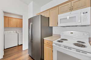Kitchen featuring white appliances, independent washer and dryer, wood finished floors, light brown cabinetry, and light countertops