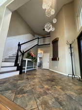 Entryway with an inviting chandelier, a high ceiling, stone tile floors, stairway, and baseboards