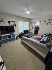 Bedroom with carpet, a ceiling fan, visible vents, and a textured ceiling