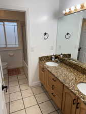 Bathroom with toilet, baseboards, a sink, tile patterned flooring, and double vanity