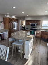 Kitchen featuring light stone countertops, light wood-style flooring, a textured ceiling, a center island, and stainless steel appliances