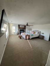 Carpeted bedroom featuring baseboards, a glass covered fireplace, a ceiling fan, and a textured ceiling
