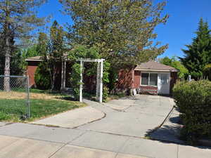 View of property hidden behind natural elements featuring a front lawn, brick siding, and fence