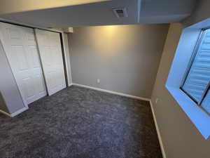 Unfurnished bedroom featuring baseboards, a closet, dark colored carpet, and visible vents