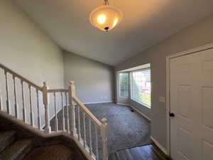 Carpeted foyer entrance with baseboards and vaulted ceiling