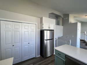 Kitchen with freestanding refrigerator, white cabinets, dark wood-style flooring, dishwasher, and light stone counters