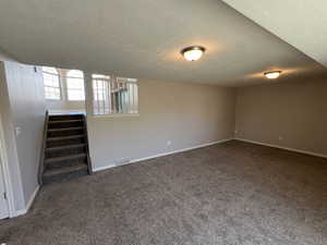 Below grade area with carpet flooring, stairway, visible vents, and a textured ceiling