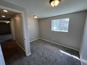 Empty room featuring a textured ceiling, baseboards, and dark carpet