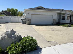 View of front of house with stone siding, driveway, an attached garage, and fence