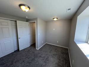 Unfurnished bedroom featuring a closet, a textured ceiling, baseboards, visible vents, and dark carpet