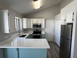 Kitchen with a peninsula, a sink, stainless steel appliances, light stone countertops, and lofted ceiling