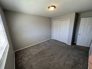 Unfurnished bedroom with baseboards, a closet, dark colored carpet, and a textured ceiling