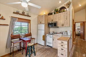 Kitchen with light wood-style flooring, light brown cabinets, vaulted ceiling with skylight, white appliances, and light countertops