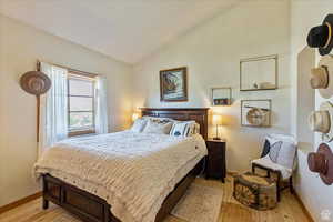 Bedroom with baseboards, light wood-type flooring, and vaulted ceiling