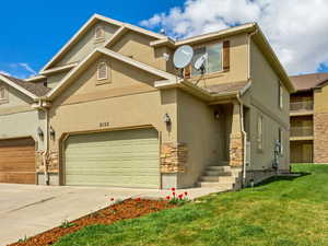 View of front of house featuring driveway, stucco siding, stone siding, and a front yard