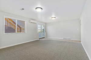 Basement family room featuring visible vents, a wall mounted AC, light carpet, and french doors