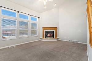 Living room featuring visible vents, carpet flooring, high vaulted ceiling, a gas fireplace, and a ceiling fan