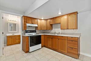 Basement kitchen with white range with electric cooktop, a sink, light countertops, baseboards, and under cabinet range hood