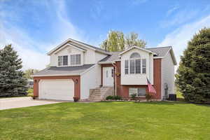 Split foyer home featuring driveway, brick siding, a garage, roof with shingles, and a front lawn