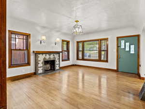 Unfurnished living room featuring a textured ceiling, light wood-type flooring, baseboards, a chandelier, and healthy amount of natural light