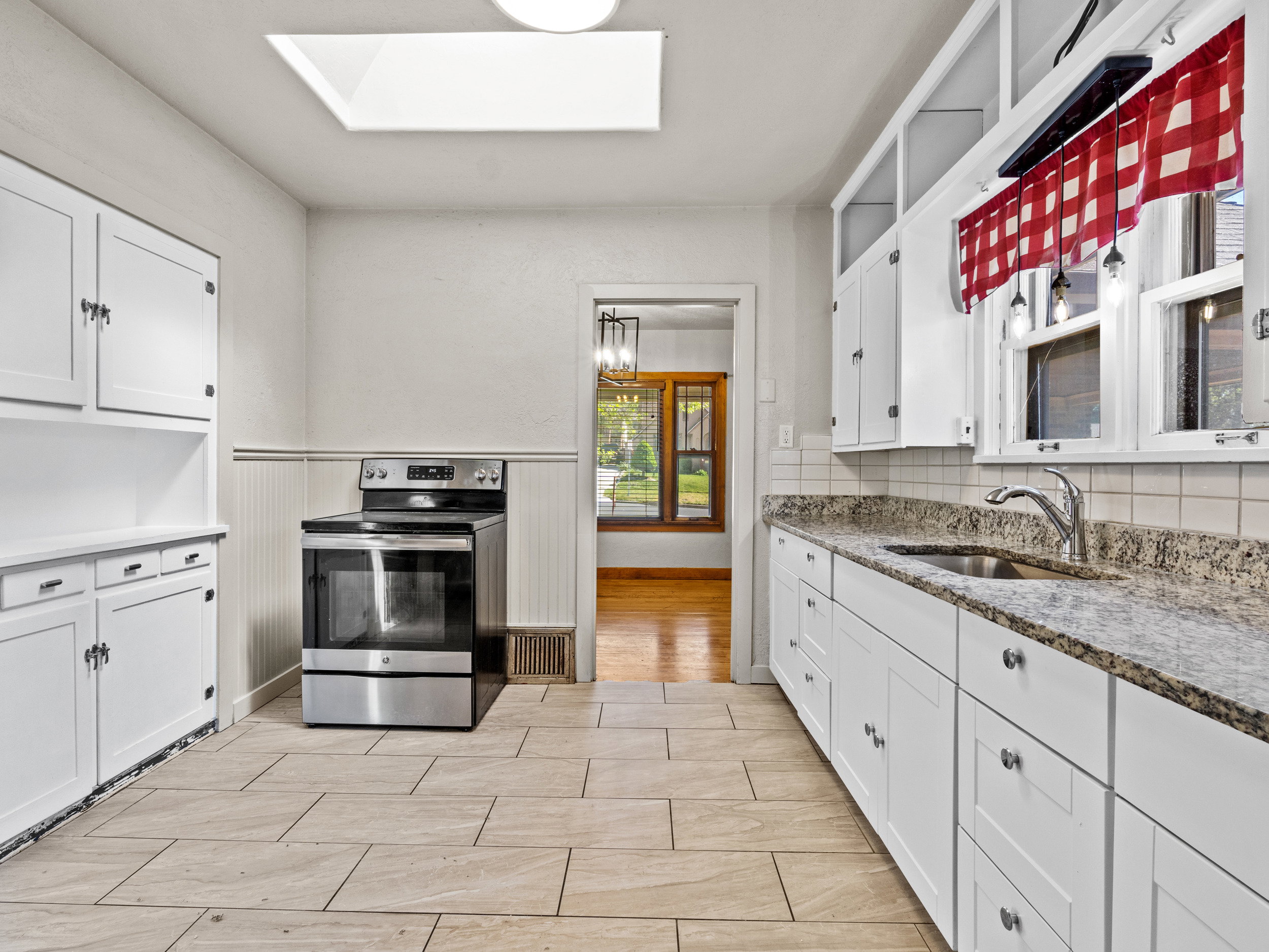 Kitchen with stainless steel range with electric stovetop, a skylight, a sink, white cabinets, and a wainscoted wall