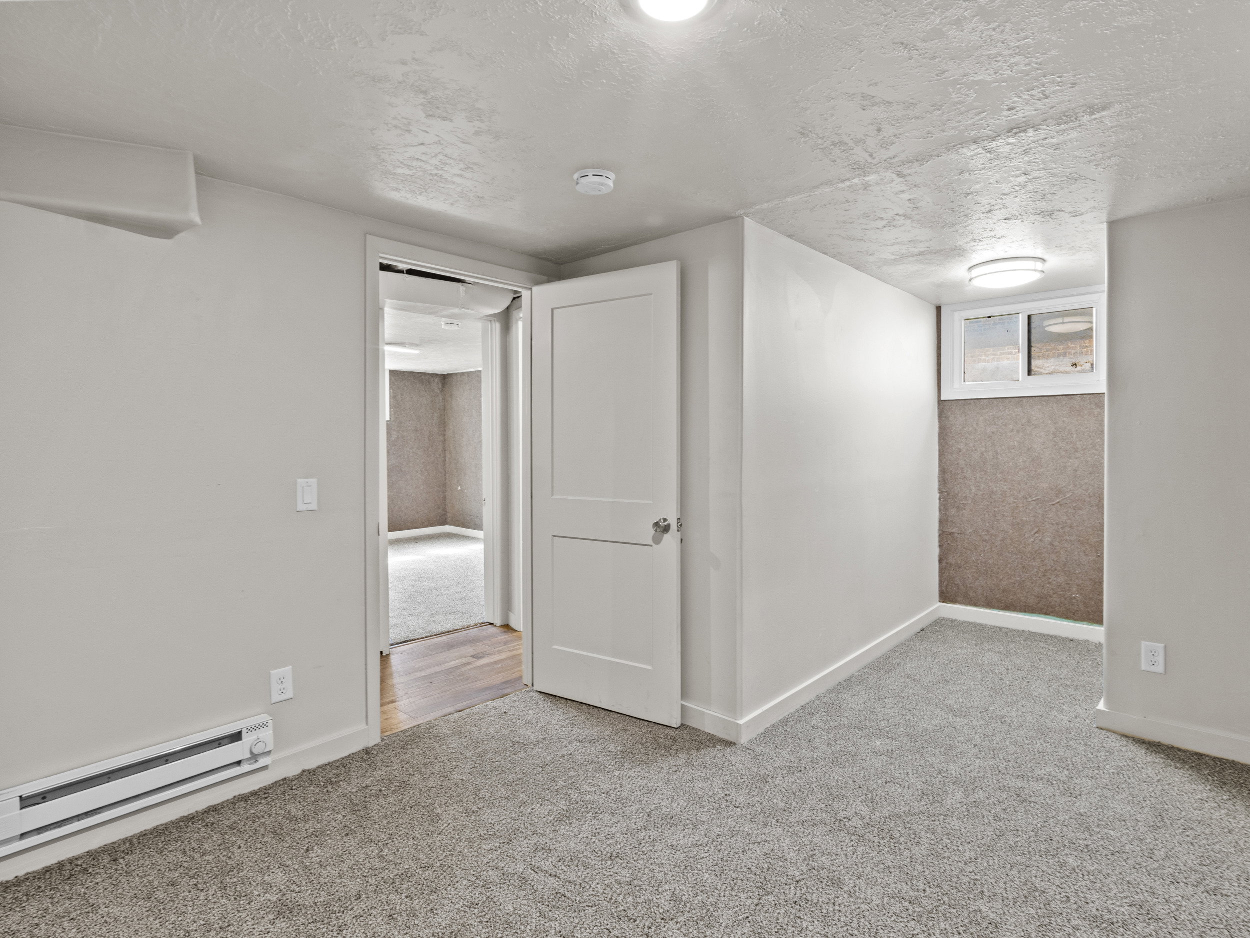 Below grade bedroom with a baseboard radiator, a textured ceiling, carpet, and baseboards