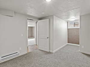 Below grade bedroom with a baseboard radiator, a textured ceiling, carpet, and baseboards