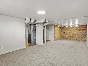 Finished below grade area featuring carpet flooring, a textured ceiling, brick wall, and baseboards