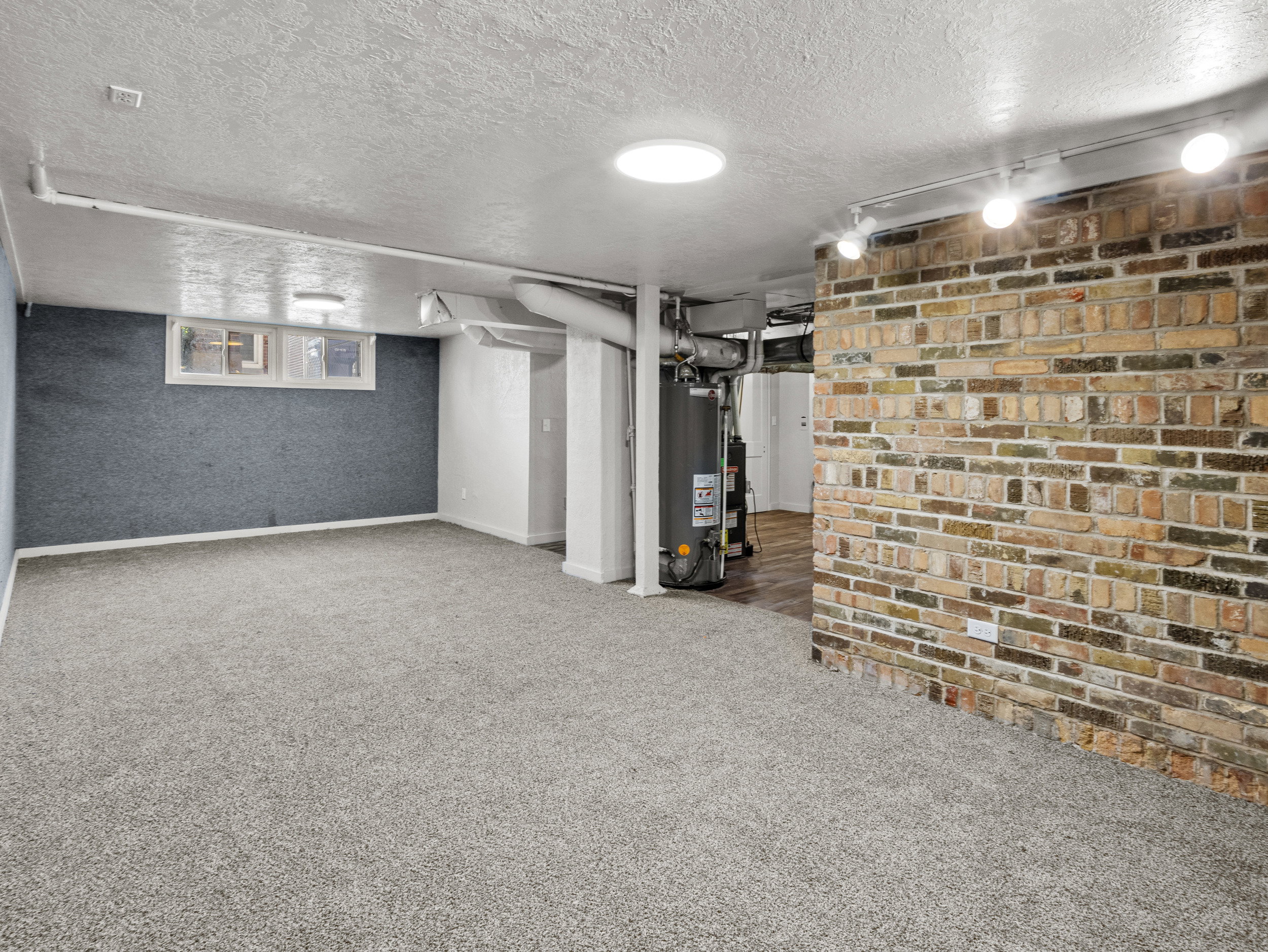 Finished below grade area with a textured ceiling, carpet floors, water heater, and baseboards