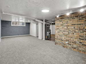Finished below grade area with a textured ceiling, carpet floors, water heater, and baseboards