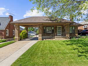View of front facade featuring driveway, a front lawn, brick siding, an attached carport, and a porch