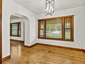 Unfurnished room featuring arched walkways, light wood-style flooring, baseboards, and a chandelier