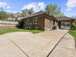 View of side of home with cooling unit, a chimney, brick siding, concrete driveway, and a mountain view